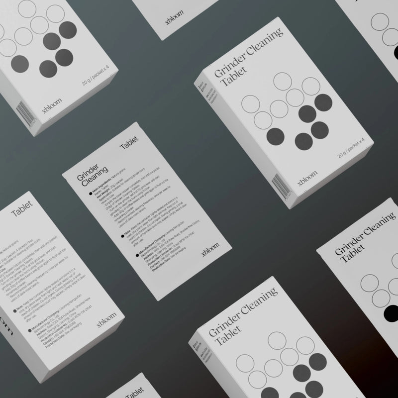 Multiple xBloom Grinder Cleaning Tablet boxes and packets arranged in a repeating pattern on a grey background, showcasing the brand's clean and professional aesthetic.