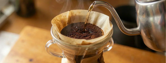 a steaming pourover coffee being brewed, hot water pouring from a gooseneck kettle over fresh grounds