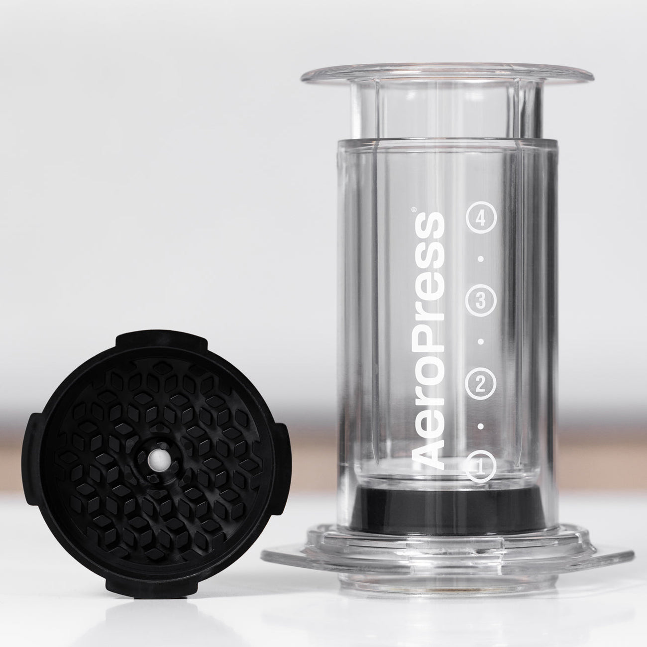 Clear AeroPress brewer with a black filter cap, showing the disassembled components