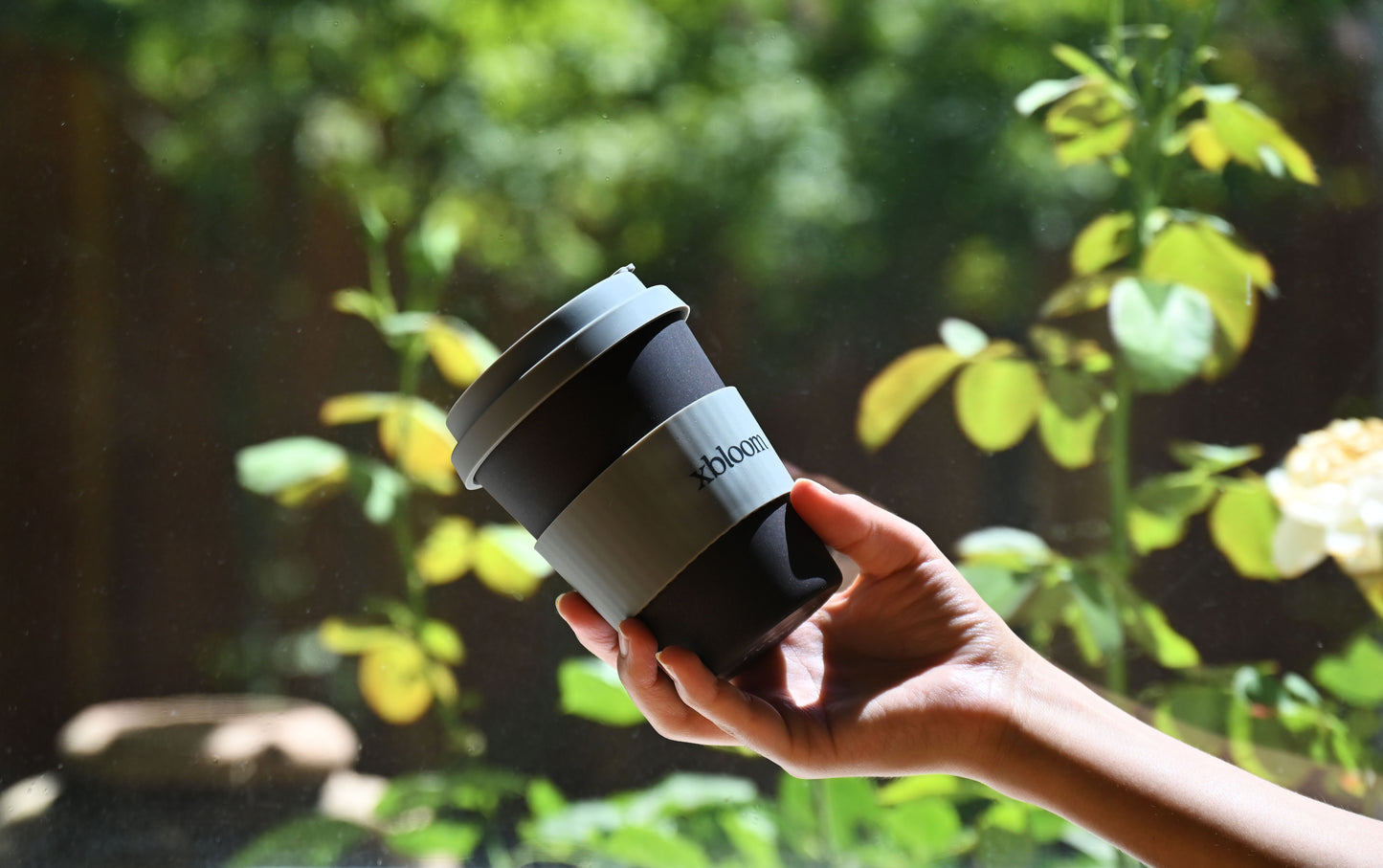 xBloom reusable travel coffee cup being held in a hand, outdoors