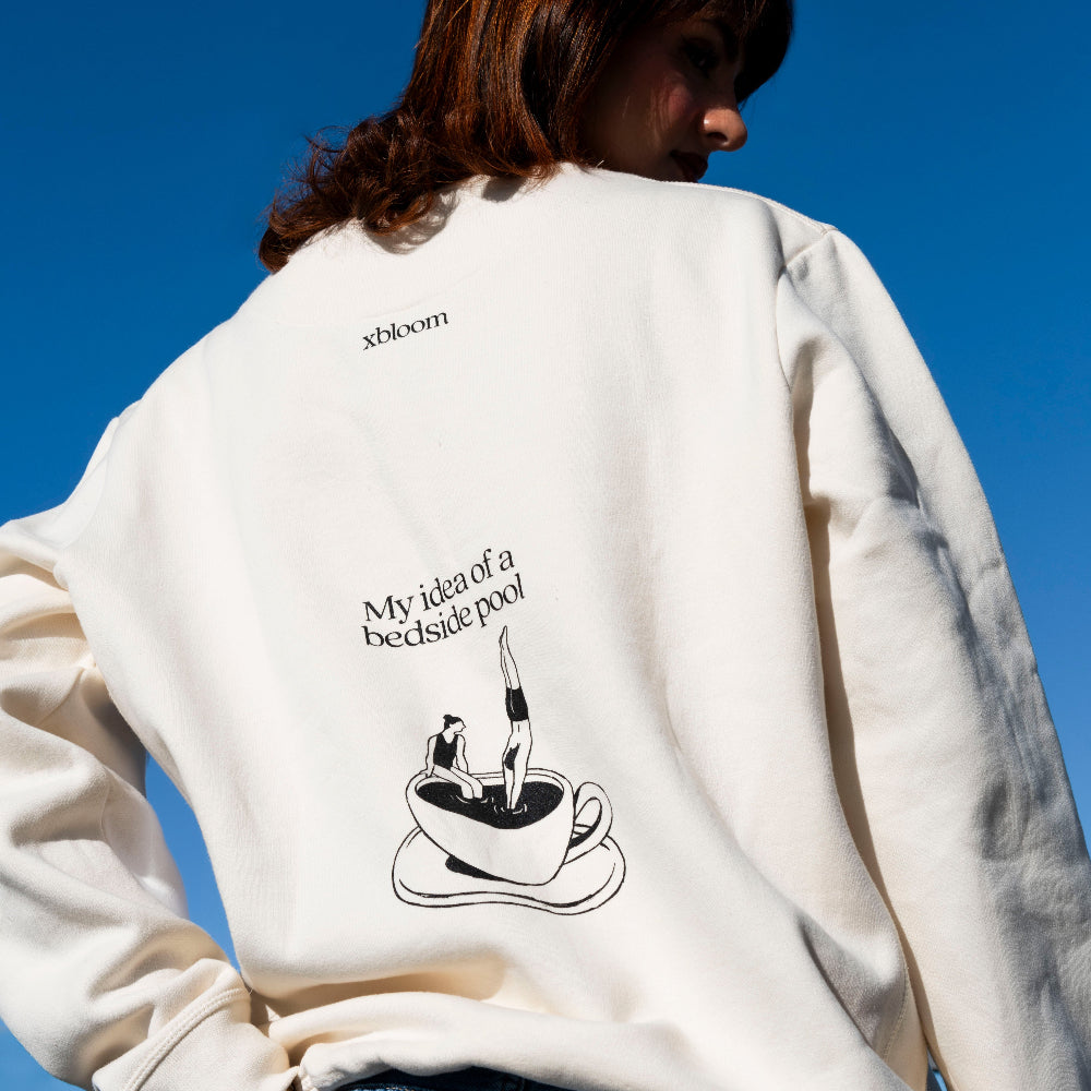 Person wearing a white sweatshirt with a graphic and text on the back against a blue sky.