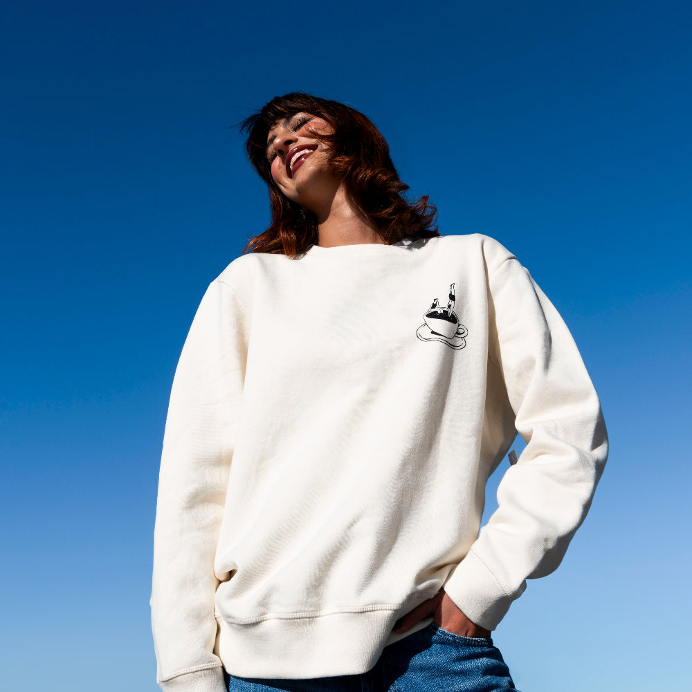 Person wearing a white sweatshirt with a small graphic against a clear blue sky