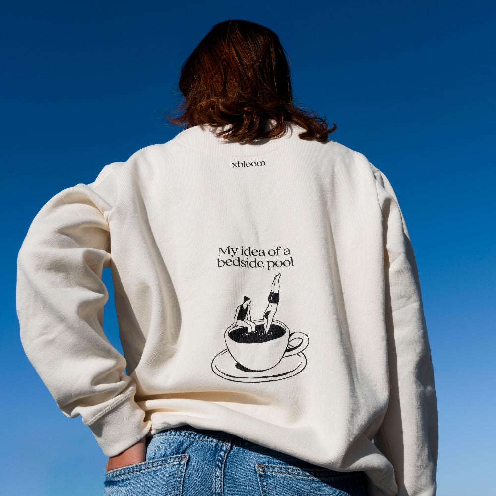 Person wearing a white sweatshirt with a graphic and text against a clear blue sky