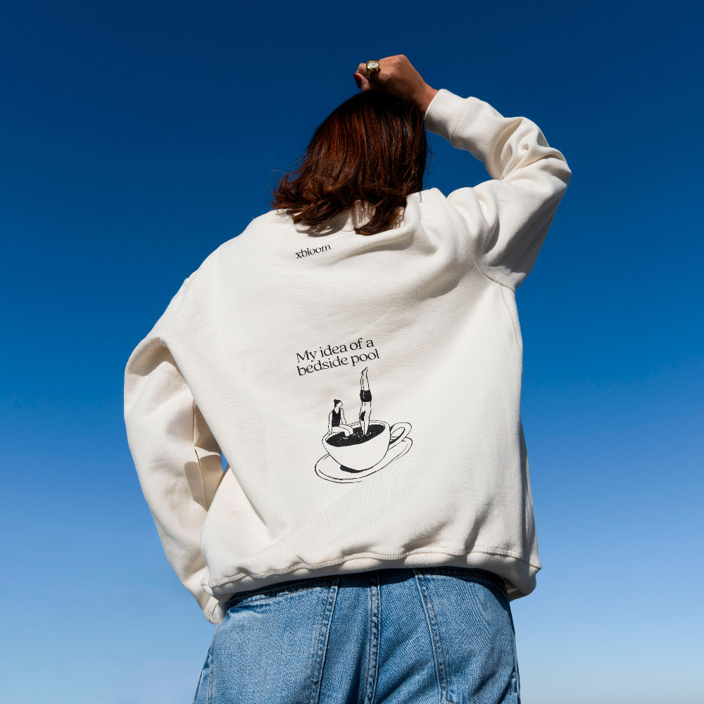 Person wearing a white sweatshirt with a graphic design against a clear blue sky
