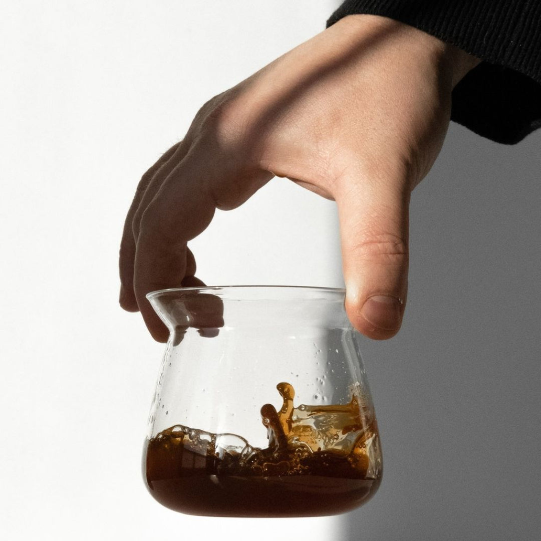 Glass coffee carafe with splashing coffee, held by hand
