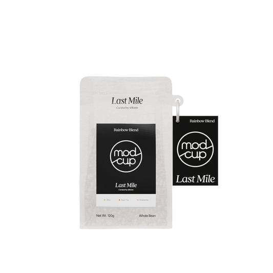 A 120g pouch of Mod Cup Last Mile Rainbow Blend whole bean coffee next to a matching black hangtag, shown on a plain white background.