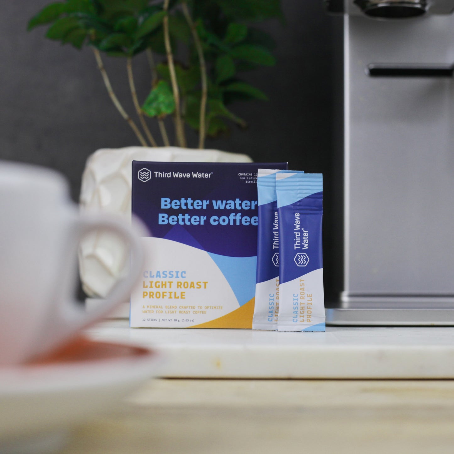 Third Wave Water Classic Light Roast coffee mineral profile box and single-serve packets, displayed on a kitchen counter with a coffee cup and xbloom coffee machine in the background