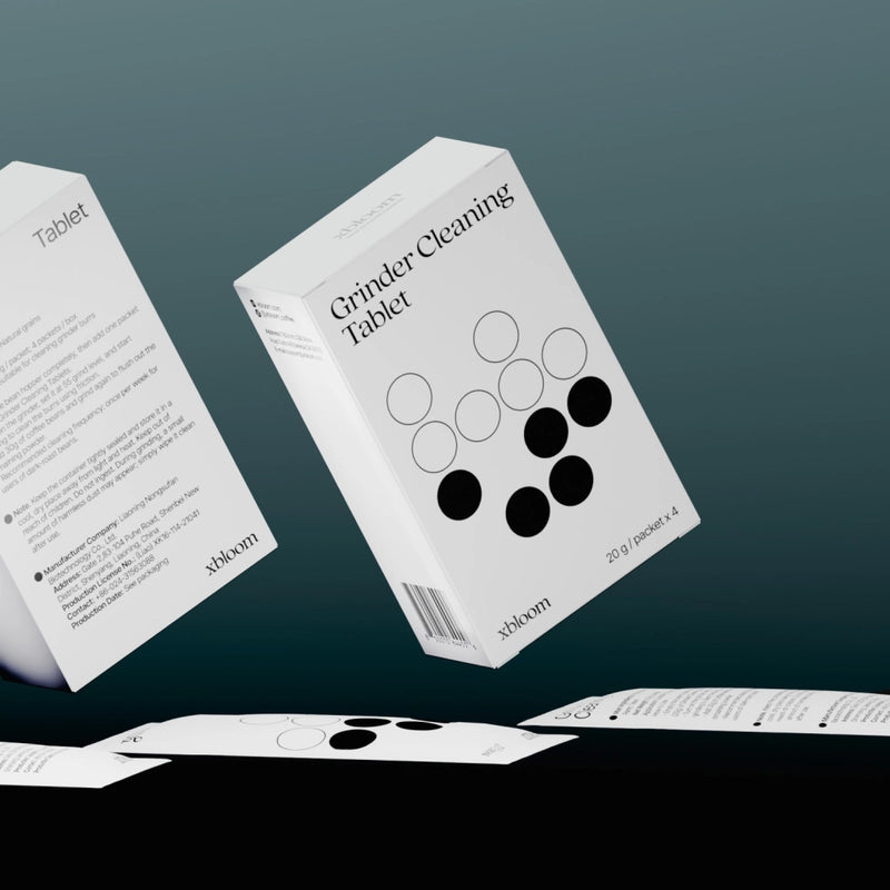 A creative layout showing the front and back of the xBloom Grinder Cleaning Tablet box alongside individual packets, highlighting the product's natural grain ingredients and usage instructions.